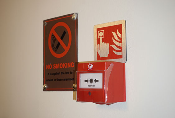red Fire Alarm on a white wall next to a silver no smoking sign